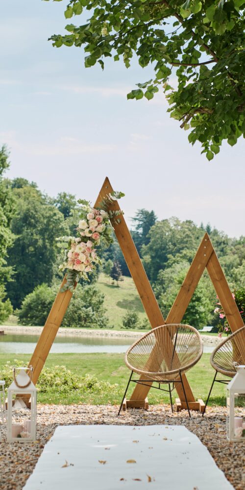 Photo cérémonie laïque avec une arche montagne en bois, des fauteils en corde pour les mariés et une allées blanches en tapis par Ma Déco Chic